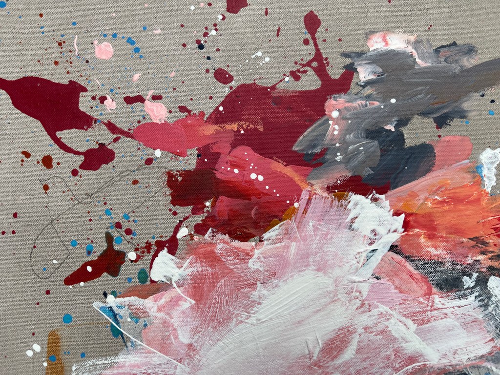 Close up view of pink, red and white paint with splashes of colour and ink on canvas